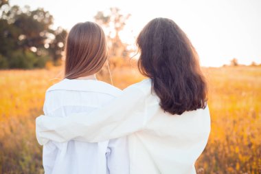 Beyaz gömlekli iki kız gün batımını seyrediyor. En iyi arkadaşlar
