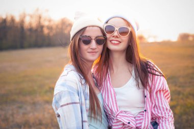 İki genç kadın gün batımında sahada durup gülümsüyor. En iyi arkadaşlar