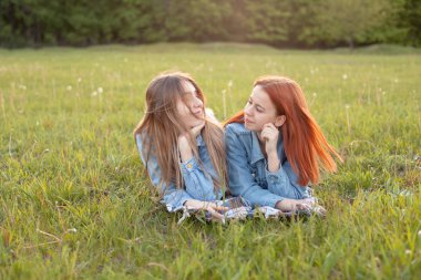 İki genç kadın çimlere uzanıp birbirlerine bakıyorlar. En iyi arkadaşlar.