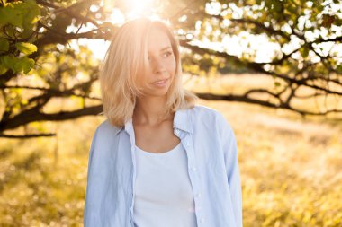 Güneş ışığının altındaki ağacın yanındaki genç kadının portresi.