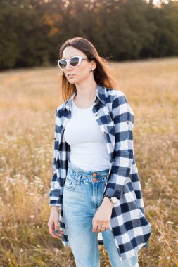 Güneş gözlüklü genç bir kadın sonbahar tarlasında yürüyor..