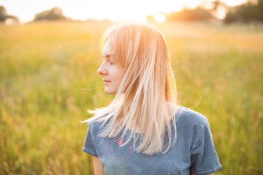 Sarışın, güzel genç bir kadın gün batımının ışığında dışarıda duruyor..
