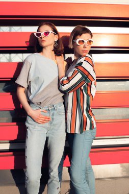 Turuncu arka planda iki şık genç kadın poz veriyor.