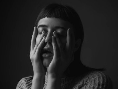 Yüzünde elleri olan üzgün genç bir kadın. Siyah ve beyaz. Kapat.