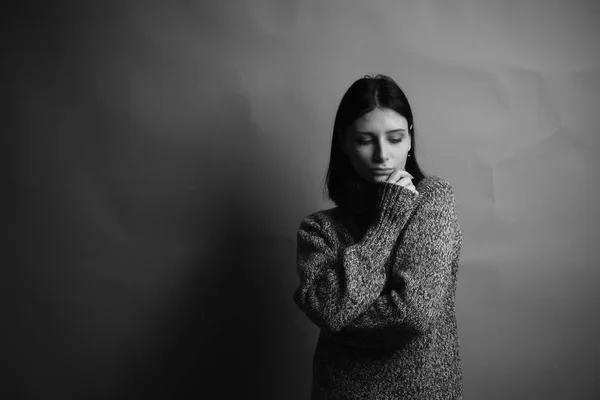 Sad young woman in sweater on gray background. Black and white