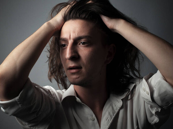 Worried young man with long hair on gray background. Studio portrait