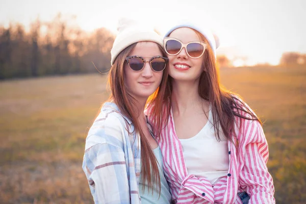 İki genç kadın gün batımında sahada durup gülümsüyor. En iyi arkadaşlar