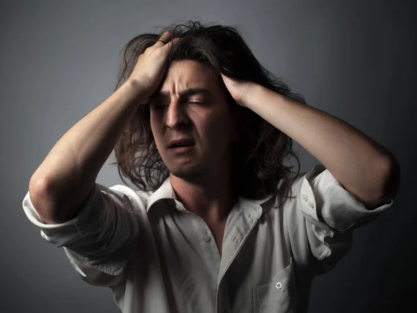 Worried young man with long hair on gray background. Studio portrait