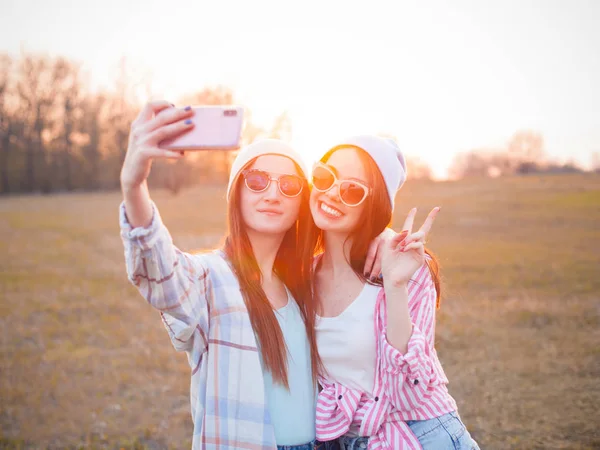 Gün batımında iki kız dışarıda selfie çekiyor.