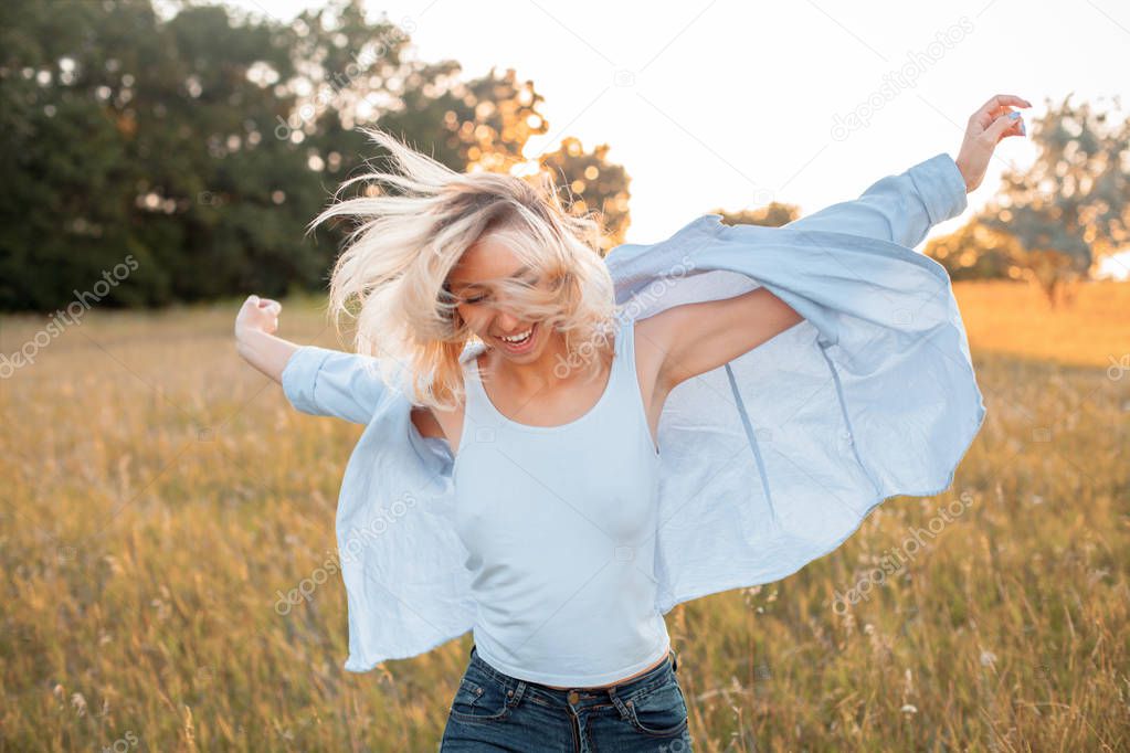 Happy young woman walking on the field at sunset.