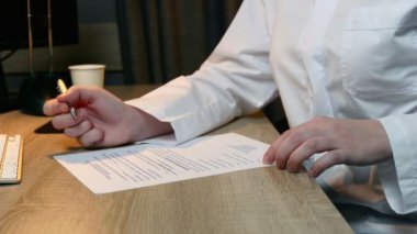 Kadın bilim adamı beyaz üniformalı bir masada oturan bir test yazıyor. Eller yakın çekim.