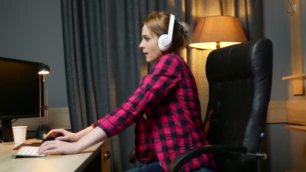 Jeune femme heureuse dans les écouteurs écoute de la musique et danse assis dans la chaise de bureau, se détendre après le travail . — Video