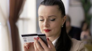 Güzel bir kadın internet üzerinden akıllı telefon alışverişi yapıyor ve ev hayatı tarzı kredi kartı kullanıyor.