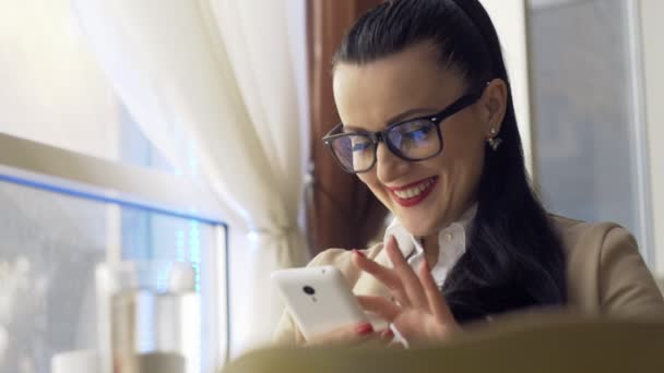 Mujer usando la aplicación en el teléfono inteligente en la cafetería bebiendo café sonriendo y mensajes de texto en el teléfono móvil. Hermosa joven multicultural casual profesional femenino en el teléfono móvil . — Vídeo de stock