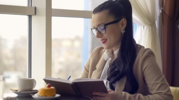 Stijlvolle jong meisje schrijft in het dagboek in het café — Stockvideo