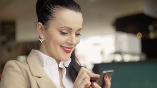 Mulher usando aplicativo no smartphone no café bebendo café sorrindo e mensagens de texto no telefone celular. Bela multicultural jovem casual profissional feminino no telefone móvel . — Vídeo de Stock