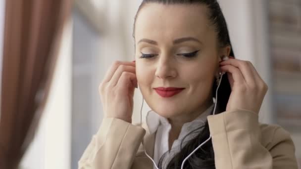 Mujer joven usando la tableta en la cafetería con auriculares — Vídeo de stock