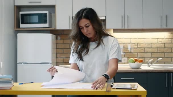 La arquitecta está trabajando con papeles sentados en la cocina en casa. . — Vídeo de stock