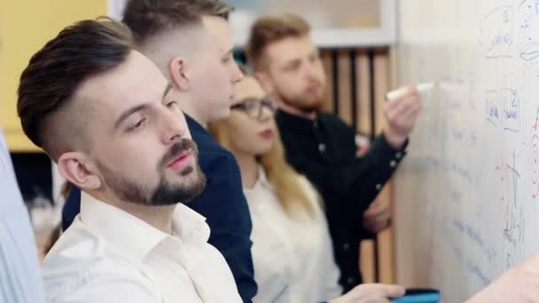 Brainstorming dans le bureau. Des collègues discutent du problème et prennent des notes sur un tableau blanc . — Video