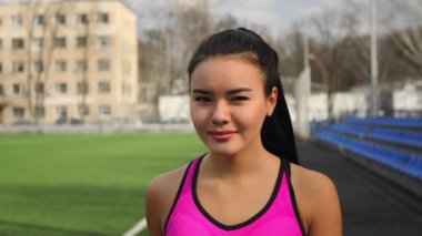 Asyalı genç sportif kız elinde su şişe ile eğitimden sonra stadyum üzerinde yürüyor.
