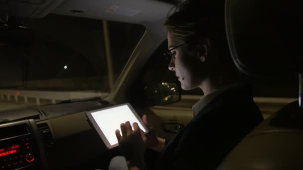 Бізнес-леді в машині використовує планшет для роботи. Вона їде в машині на нічній дорозі . — стокове відео