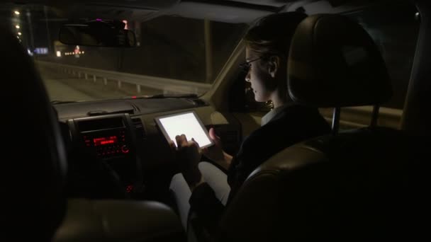 Бізнес-леді в машині використовує планшет для роботи. Вона їде в машині на нічній дорозі . — стокове відео
