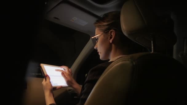 Zakenvrouw in de auto maakt gebruik van een tablet voor werk. Ze rijdt in de auto op de weg van de nacht. — Stockvideo