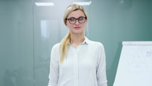Молодая блондинка в офисной одежде и очках смотрит в камеру и улыбается . — стоковое видео