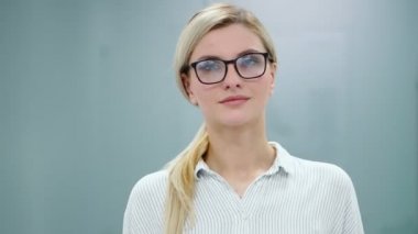 Ofis kıyafetleri ve gözlüklü genç sarışın iş kadını kameraya bakıyor ve gülümsüyor..