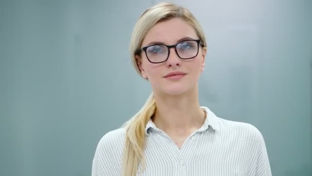 Junge blonde Geschäftsfrau in Bürokleidung und Brille blickt in die Kamera und lächelt. — Stockvideo
