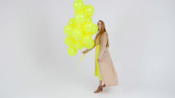 Mädchen in gelbem Rock mit gelben Luftballons in den Händen posiert vor hellem Hintergrund vor der Kamera. — Stockvideo