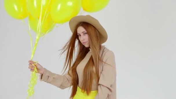 Meisje in gele rok met gele ballonnen in handen is poseren op de camera op lichte achtergrond. — Stockvideo