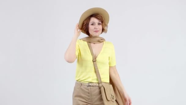 Mladá žena ve žluté blůze, béžový klobouk a šála pózuje na fotoaparátu na světlém pozadí. — Stock video