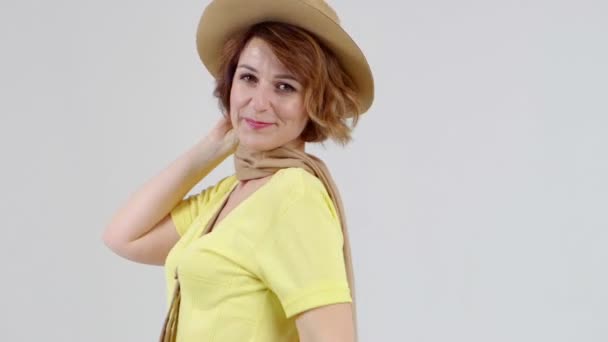 Young woman in yellow blouse, beige hat and scarf is posing at camera on light background. — Stock Video