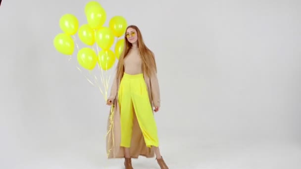 手に黄色の風船を持つ黄色のスカートの女の子は、明るい背景でカメラでポーズをとっています. — ストック動画