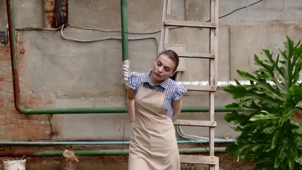 Γυναίκα κηπουρός περπατά στο θερμοκήπιο ικανοποιημένη με τη δουλειά της και να αναβάλλει τα γάντια της. — Αρχείο Βίντεο