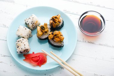 Suşi mavi tabakta, yemek çubuklarında ve soya sosunda yuvarlanıyor.