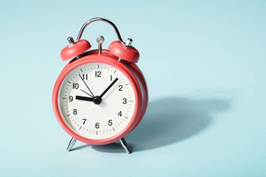 Mavi arka planda gölgesi olan kırmızı alarm saati. Dokuza yedi var.