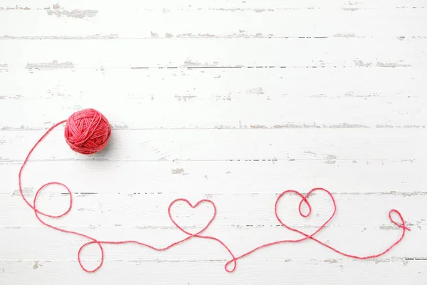 Red thread, two hearts and tangle on light wooden background