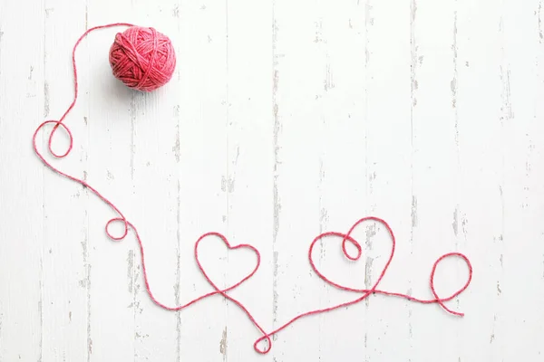 Red thread, two hearts and tangle on light wooden background