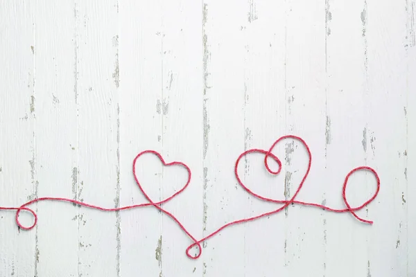 Red thread and two hearts on light wooden background