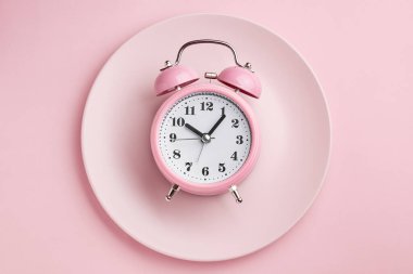 Boş pembe tabakta çalar saat. Perhiz, öğle yemeği, diyet ve kilo kaybı kavramı