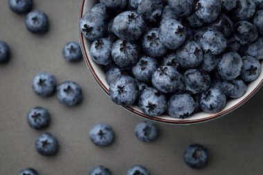Koyu gri masa arkaplanındaki kasede taze seçilmiş yaban mersini.
