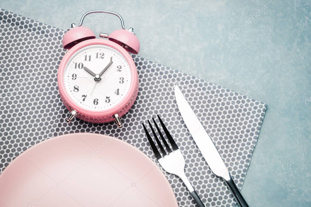 Alarm clock and plate with cutlery. Concept of intermittent fasting, lunchtime, diet and weight loss