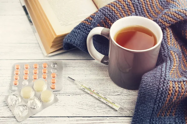 Cup of tea, book, thermometer, tablets, knitted scarf on a light background. Concept illness. Cold