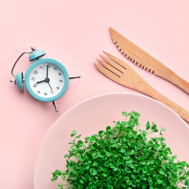 Çalar saat, çatal bıçak takımı ve pembe üzerine yeşillik. Aralıklı oruç ve diyet konsepti.