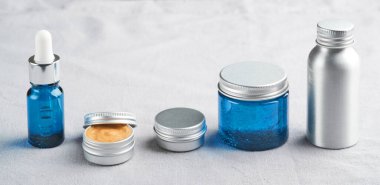 Doğal kozmetik ürünlerin keten kumaş üzerindeki metal ve cam kapları.