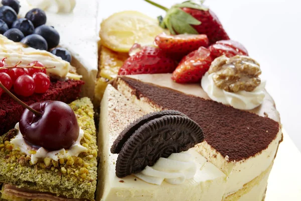 Closeup of assorted sweet homemade cakes decorated with strawberries, cranberries, blueberries, nuts, lemon, cherry and chocolate cookie, isolated on white background