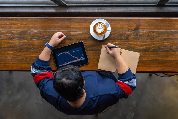 Hochwinkelaufnahme eines asiatischen Anlegers, der den Aktienmarkt auf dem Tablet überprüft — Stockfoto