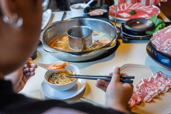 Mujer usando palillos y cuchara comiendo estilo asiático mariscos hotpot — Foto de Stock